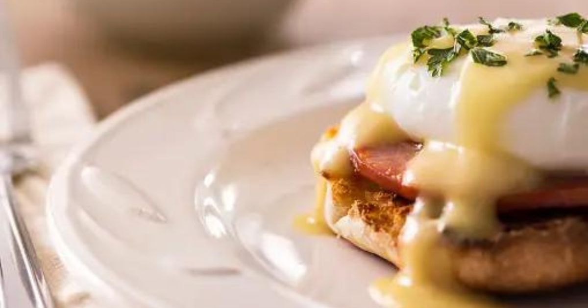 Eggs Benedict on a white plate topped with hollandaise sauce